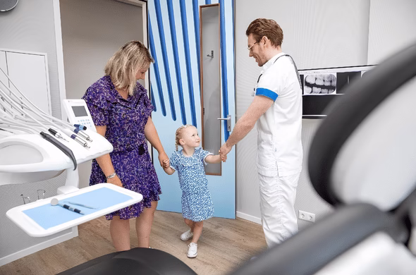 Tandarts verwelkomt een jong kind en haar begeleider in de behandelkamer.